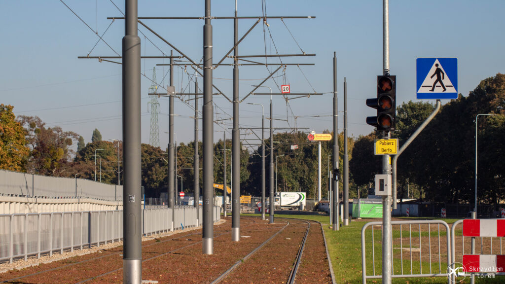 Zdjęcie pokazujące niedziałający sygnalizator z tabliczką "Pobierz berło" i  skrzynką poniżej. W tle trasa tramwajowa.